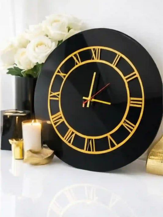 Black wall clock with gold Roman numerals on a white surface with decorative items.