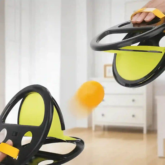 Two black and yellow steering wheel toys with a ball in the foreground, set against a blurred indoor background.