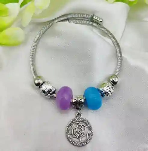Silver bracelet with colorful beads and a rose charm on a white fabric background.