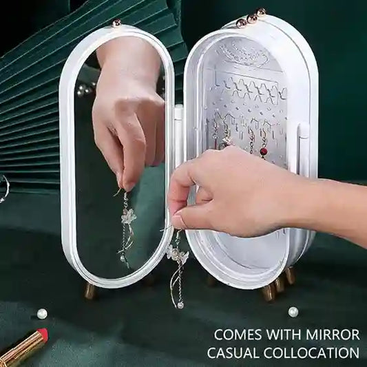 Person organizing earrings in a jewelry box with mirror on a green background