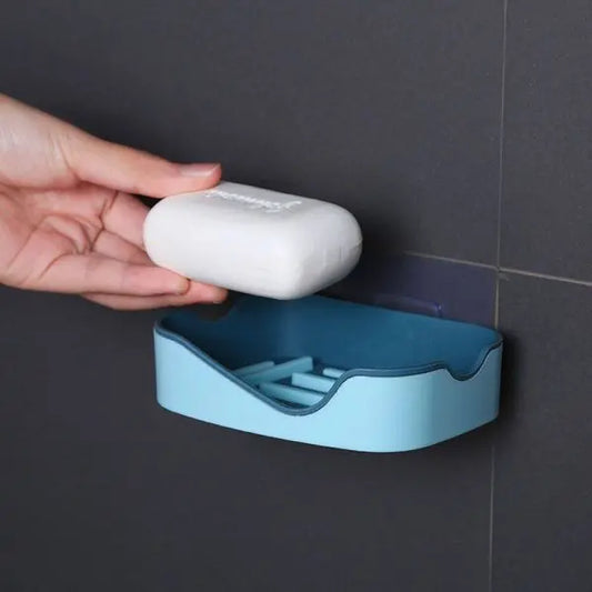 Hand placing a bar of soap into a blue soap holder against a dark tiled wall.