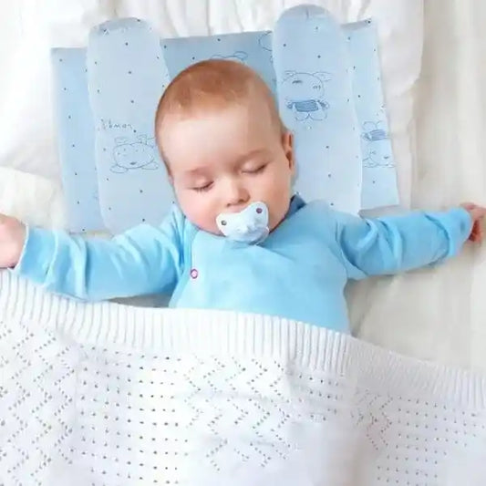 Baby in a blue outfit lying on a white blanket with a blue pillow
