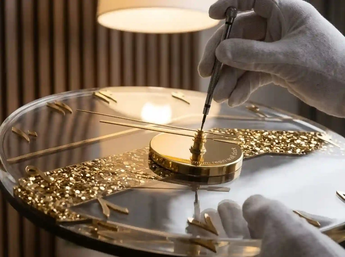 A close-up of a luxury clock being adjusted by a gloved hand using a precision tool. The clock features a clear glass face, gold-toned hands, and ornate gold accents.