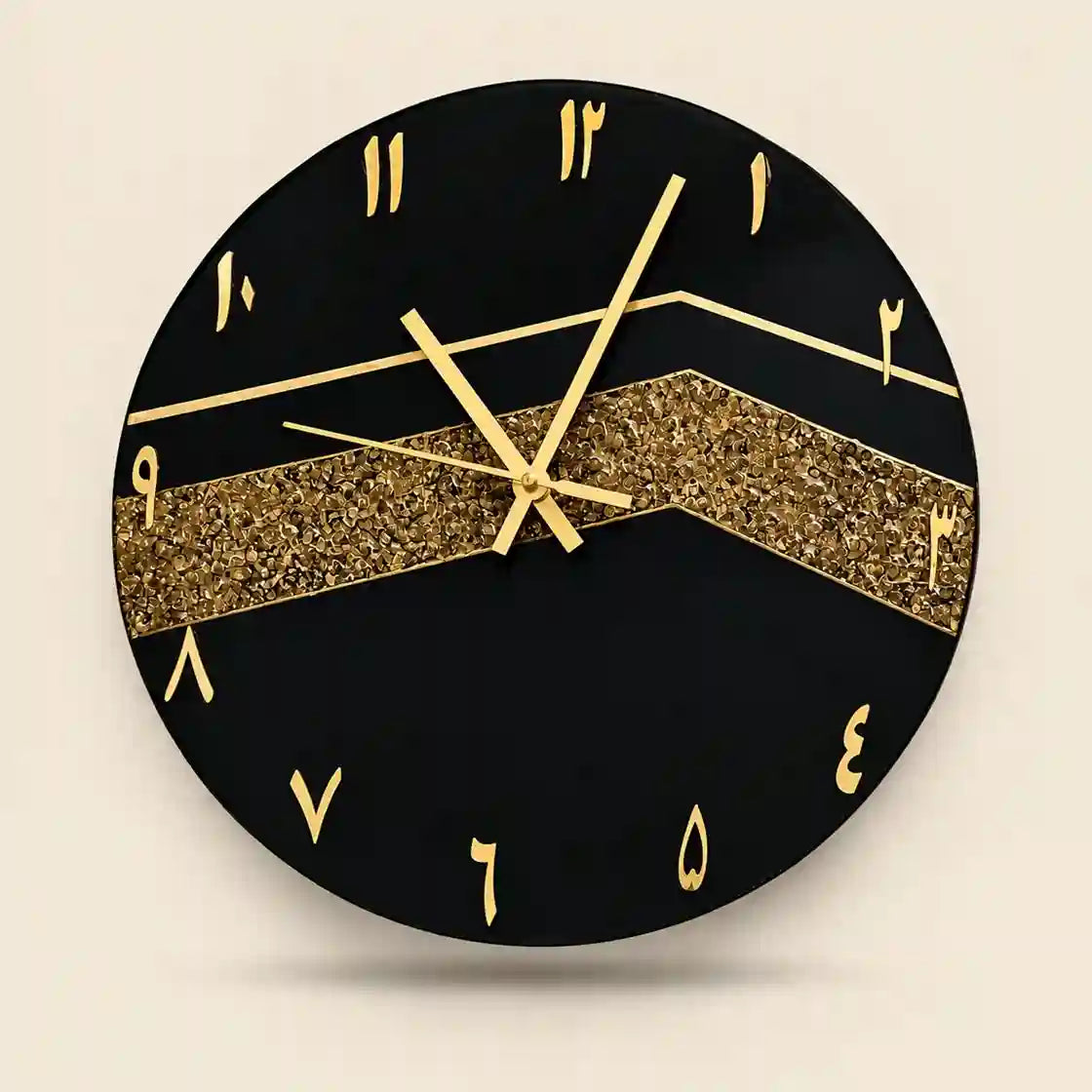 A round black wall clock with gold Arabic numeral hour markers, gold hands, and a wide glittery gold chevron stripe across the center, shown against a light beige background.