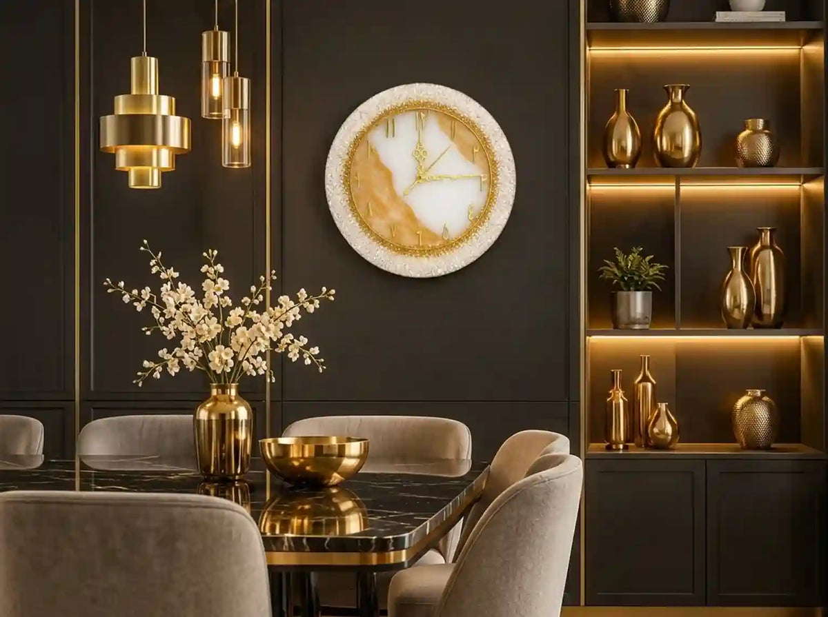 A round wall clock with a textured white and gold marble design hangs on a dark charcoal wall in a modern dining room setting with gold pendant lights, a marble table, and built-in shelves with warm lighting.
