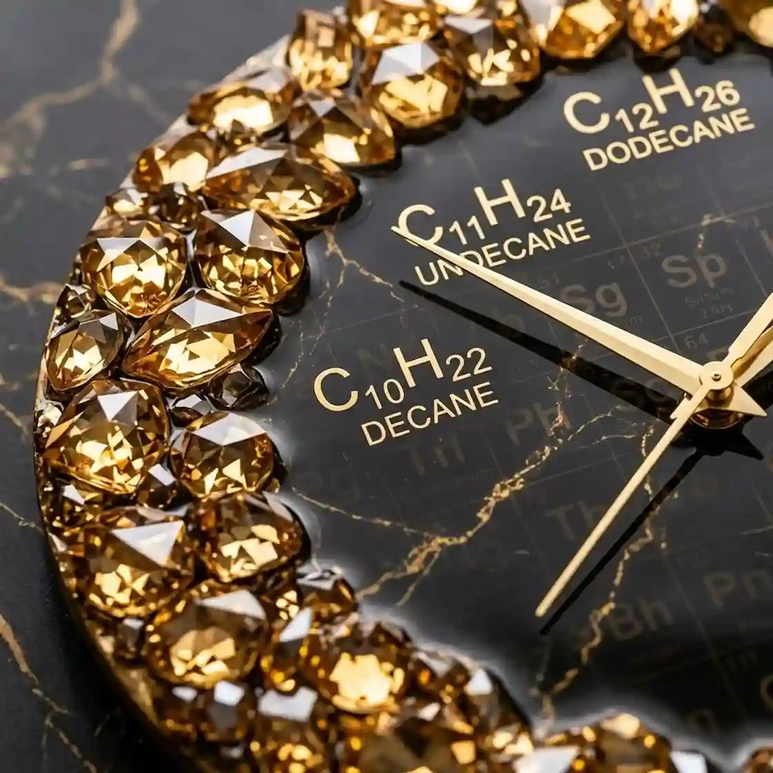 Close-up of a round wall clock with a black marble-pattern dial, gold hands, and a border of faceted gold crystals. Chemical formula time markers are printed on the dial.