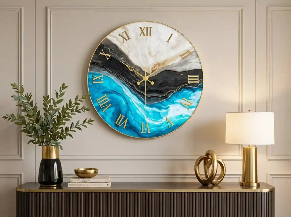 Round wall clock with a blue, black, and white marble wave design and gold Roman numerals, mounted on a beige paneled wall above a console table with a lamp and vase.