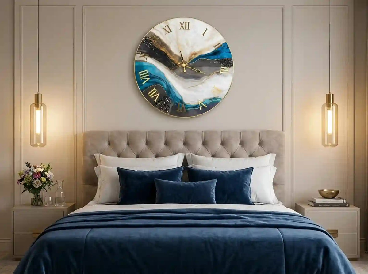 A round wall clock with an abstract blue, white, and black landscape design and gold Roman numerals, hanging above a neatly made bed in a modern bedroom.