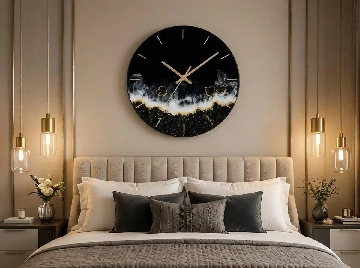 A modern round wall clock with a black background and a gold glittery wave design, hanging above a neatly made bed in a styled bedroom.