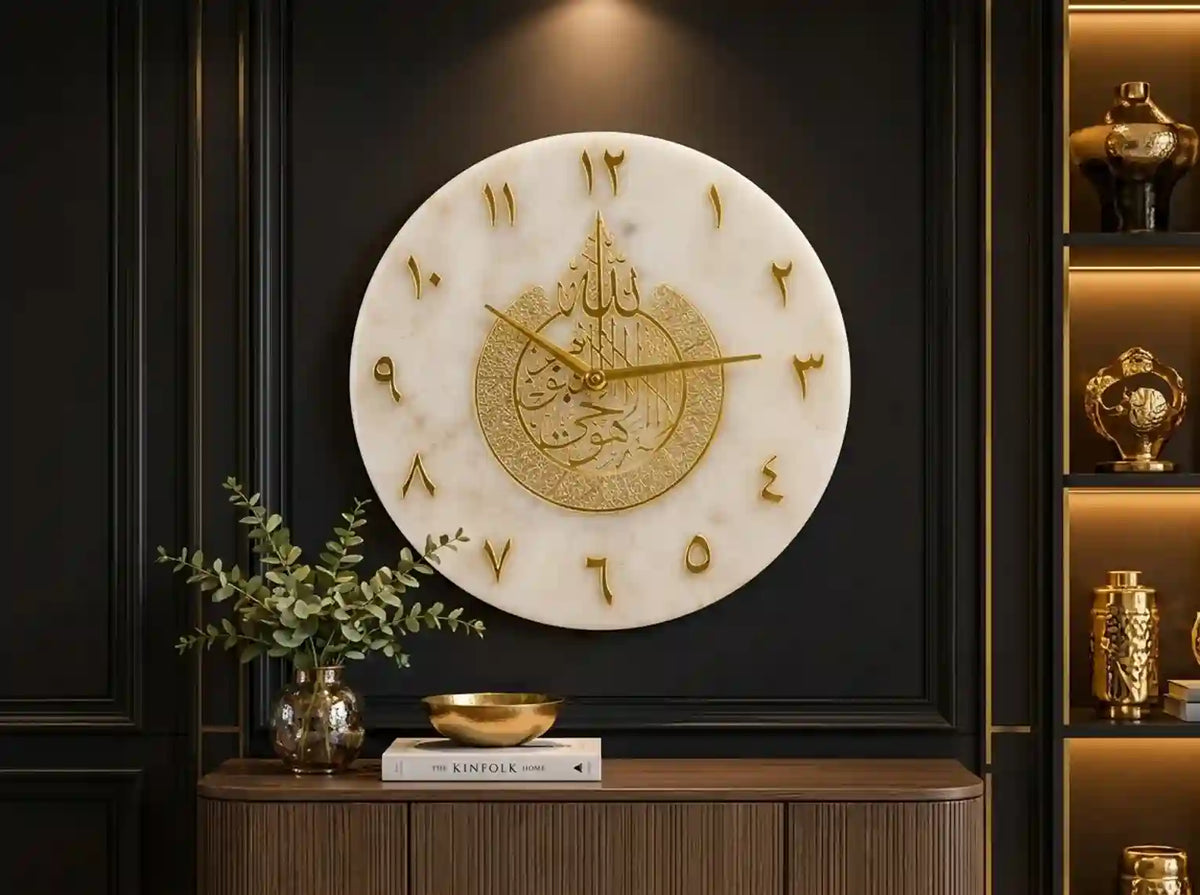 A large round wall clock with a white marble-look face, gold Arabic numeral hour markers, and ornate gold hands, mounted on a dark paneled wall above a console table with decorative items.