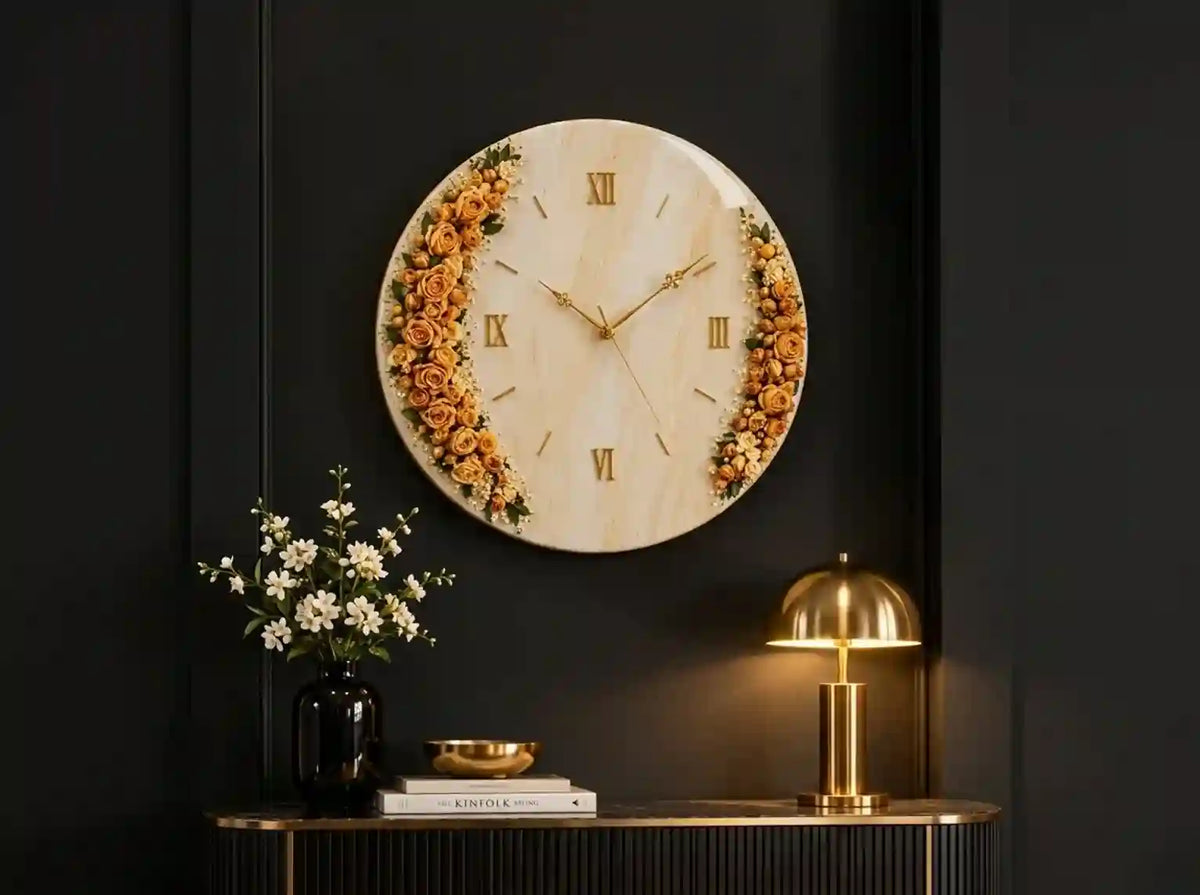A round wall clock with a light wood background and dried orange flowers framing the Roman numerals, mounted on a dark wall above a console table with a gold lamp and white flowers.