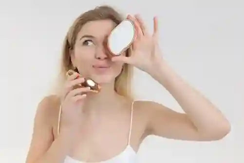 Woman holding a compact mirror to her face against a plain background