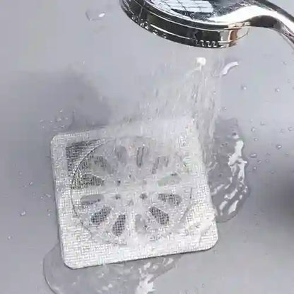 Square metal filter being rinsed under running water with a showerhead.
