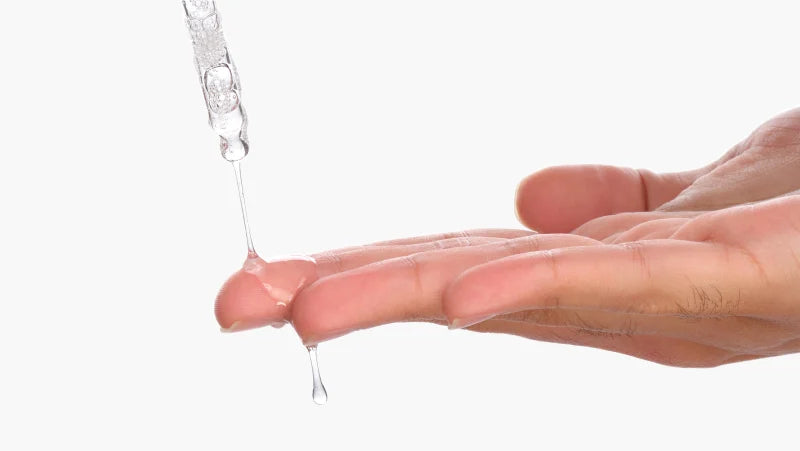 Hand holding a small amount of clear gel or cream with a dropper above it on a white background.