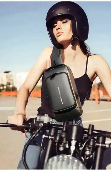 Woman riding a motorcycle wearing a black helmet and carrying a black crossbody bag.