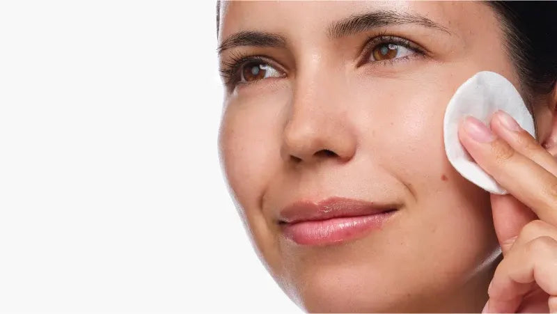 Woman applying a white patch to her face against a plain background