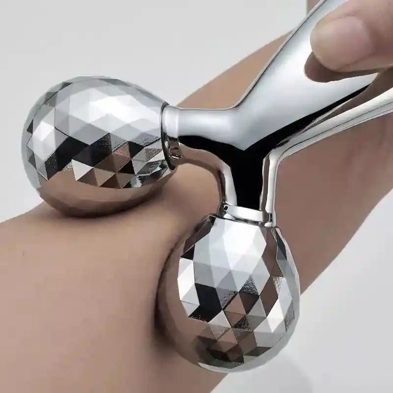 Silver facial roller held by a hand on a light background