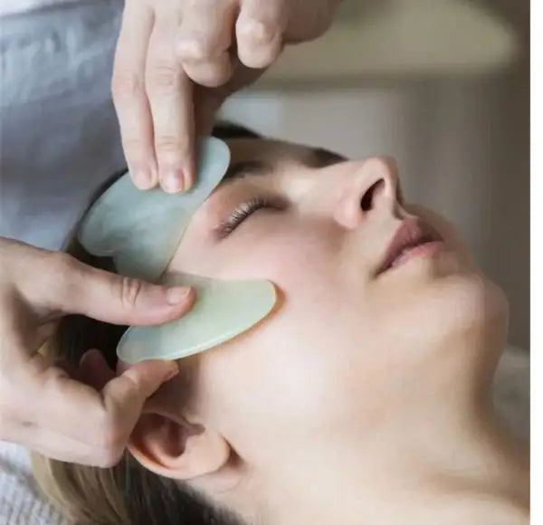 Person receiving a facial treatment with jade tools on a blurred background