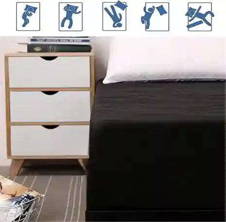 Bed with black fitted sheet and white nightstand with drawers.