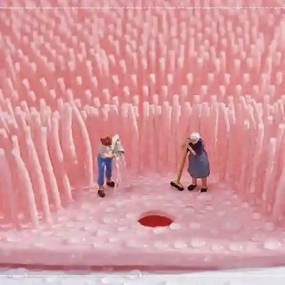 Two people standing inside a large pink foam-like structure with a small red circle at the bottom.