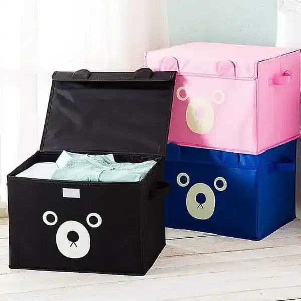 Three bear-shaped storage boxes in black, pink, and blue on a light wooden floor.