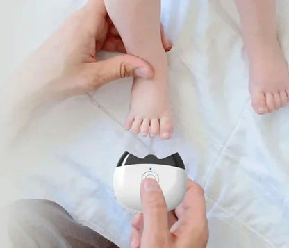 Small white device with black accents held by a hand, near a child's feet on a white blanket.