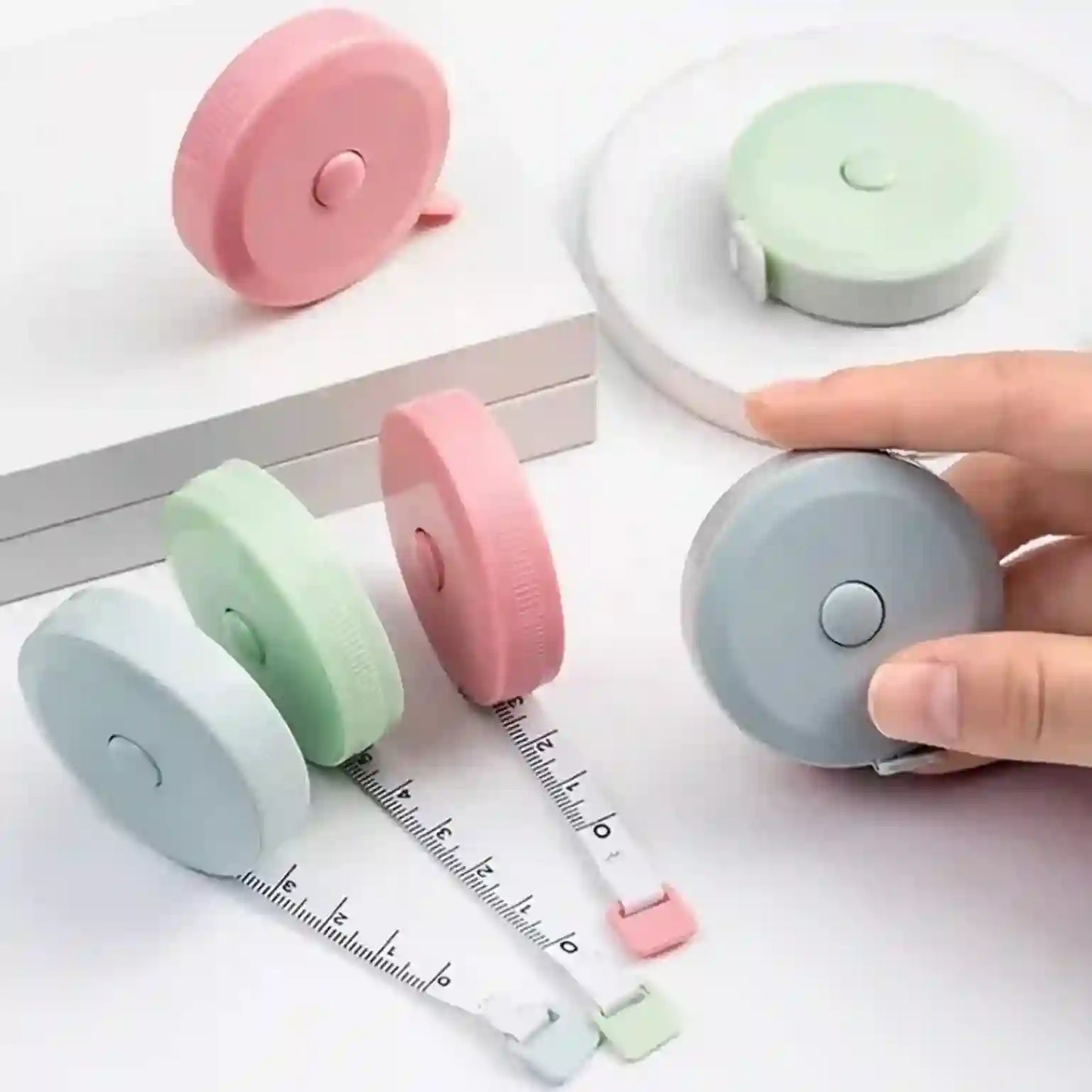 Set of colorful retractable measuring tapes on a white surface with a hand holding one.
