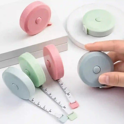 Set of colorful retractable measuring tapes on a white surface with a hand holding one.