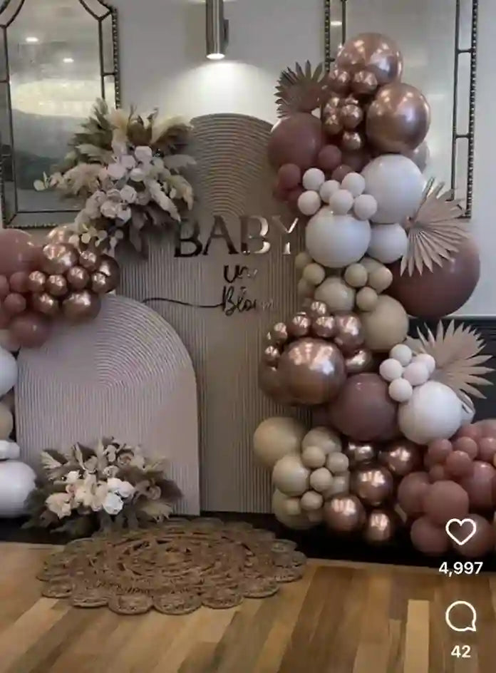 Decorative balloon arch with flowers and a 'Baby' sign in a room.