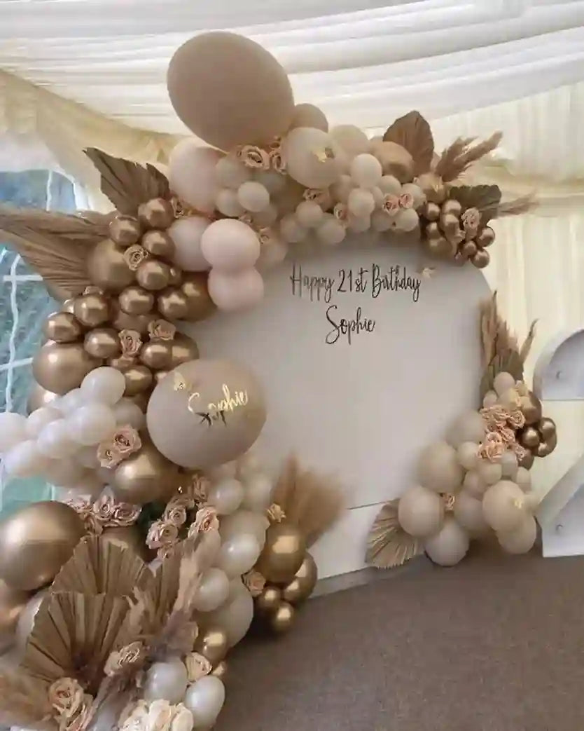 Decorative balloon arch with flowers and a personalized sign for a birthday celebration.
