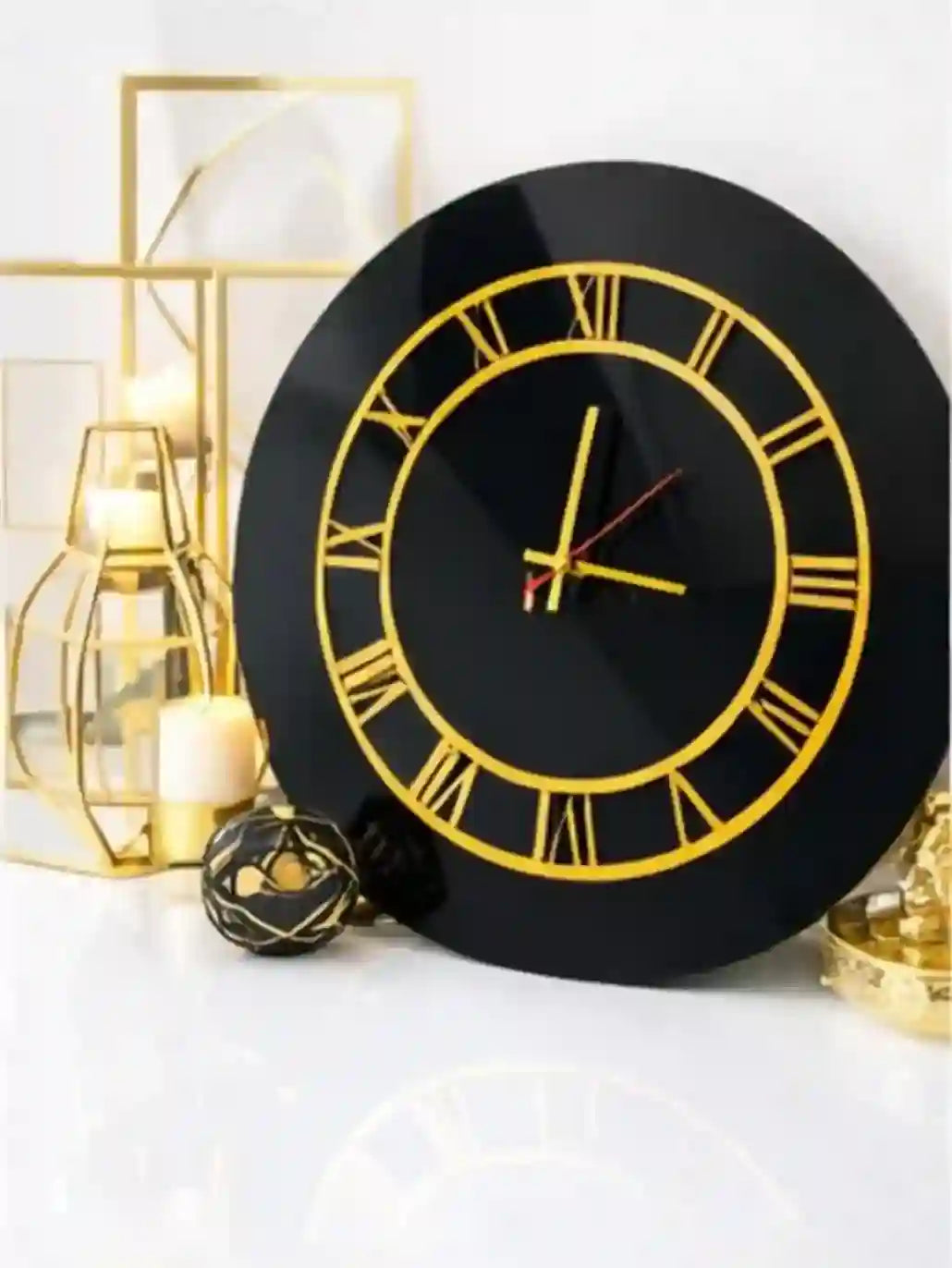 Black wall clock with gold Roman numerals on a white surface with decorative items.