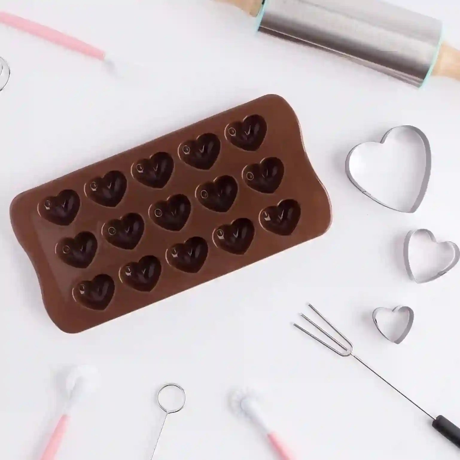 Chocolate mold with heart shapes on a white surface with baking tools.