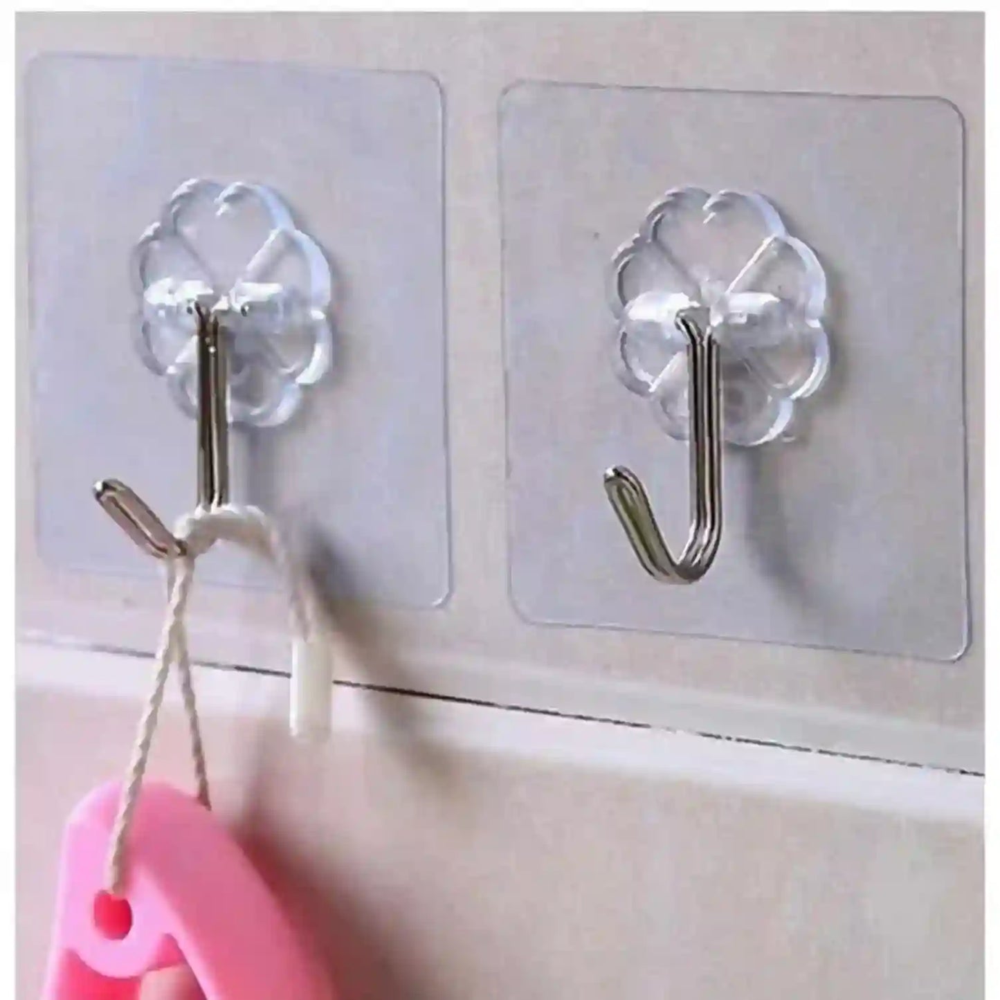 Clear adhesive hooks on a wall with a pink object hanging from one of them.