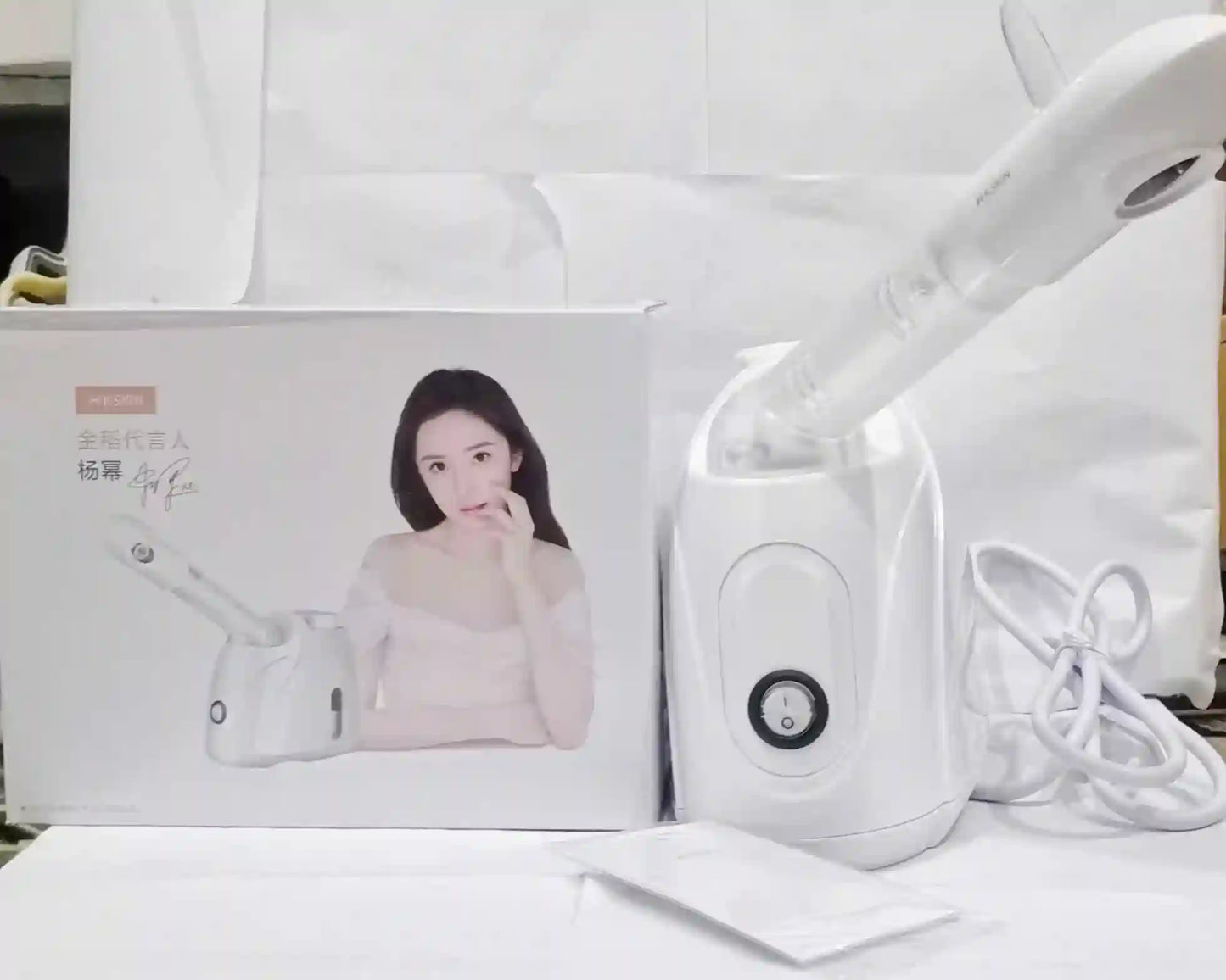 White handheld device with packaging featuring a woman's face on a white surface