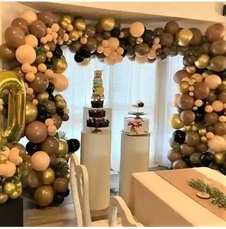 Balloon arch with gold, black, and white balloons in a room with cake stands.