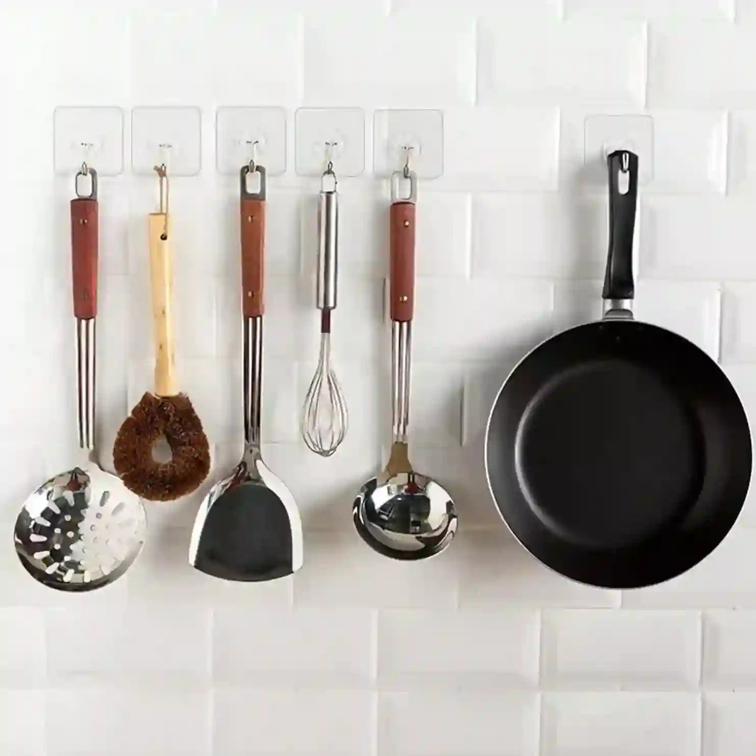 Set of kitchen utensils and a frying pan hanging on a white tiled wall.