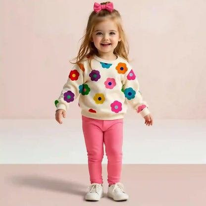 Child wearing a colorful floral sweater and pink pants on a light pink background