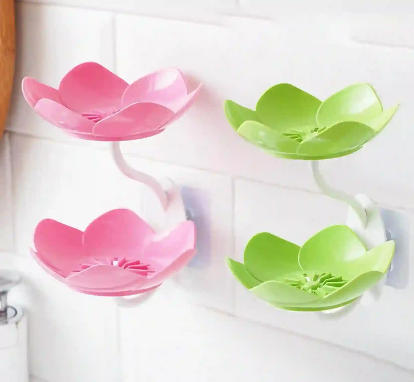 Pink and green lotus-shaped soap holders on a white tiled wall.