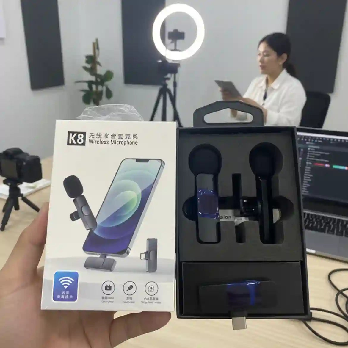 K8 wireless microphone set with packaging held by a hand, in front of a blurred office setting.