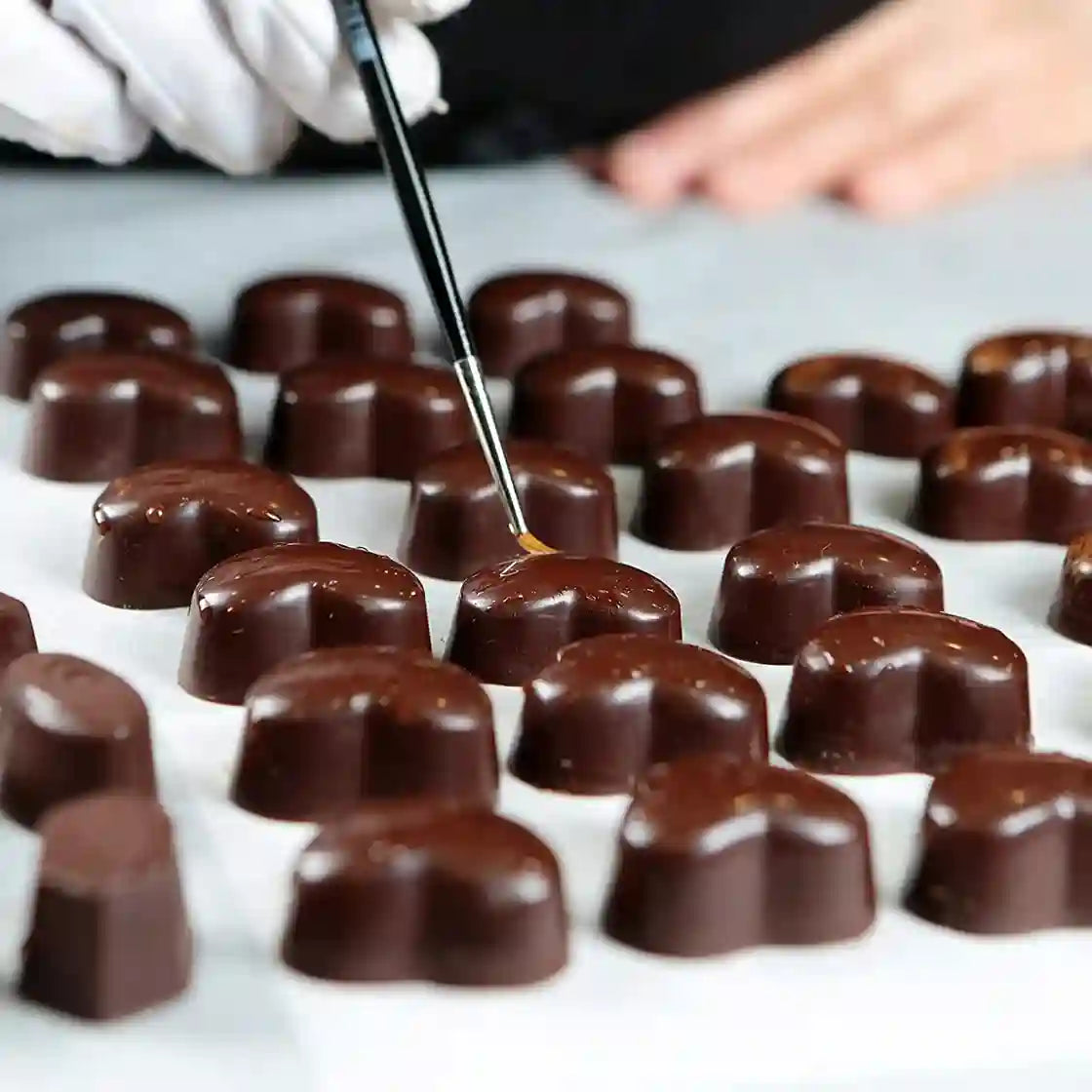 Chocolate truffles being coated with chocolate on a white surface.