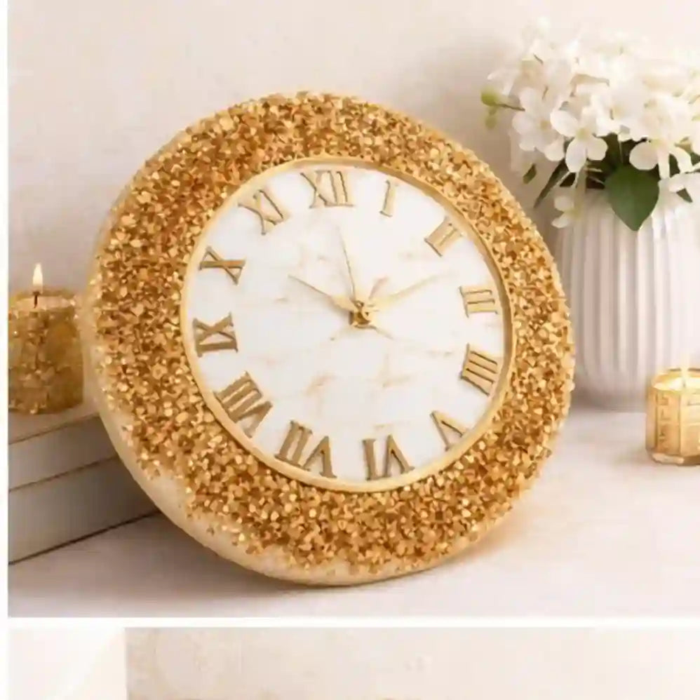 Decorative gold clock with Roman numerals on a light surface with flowers and candles in the background