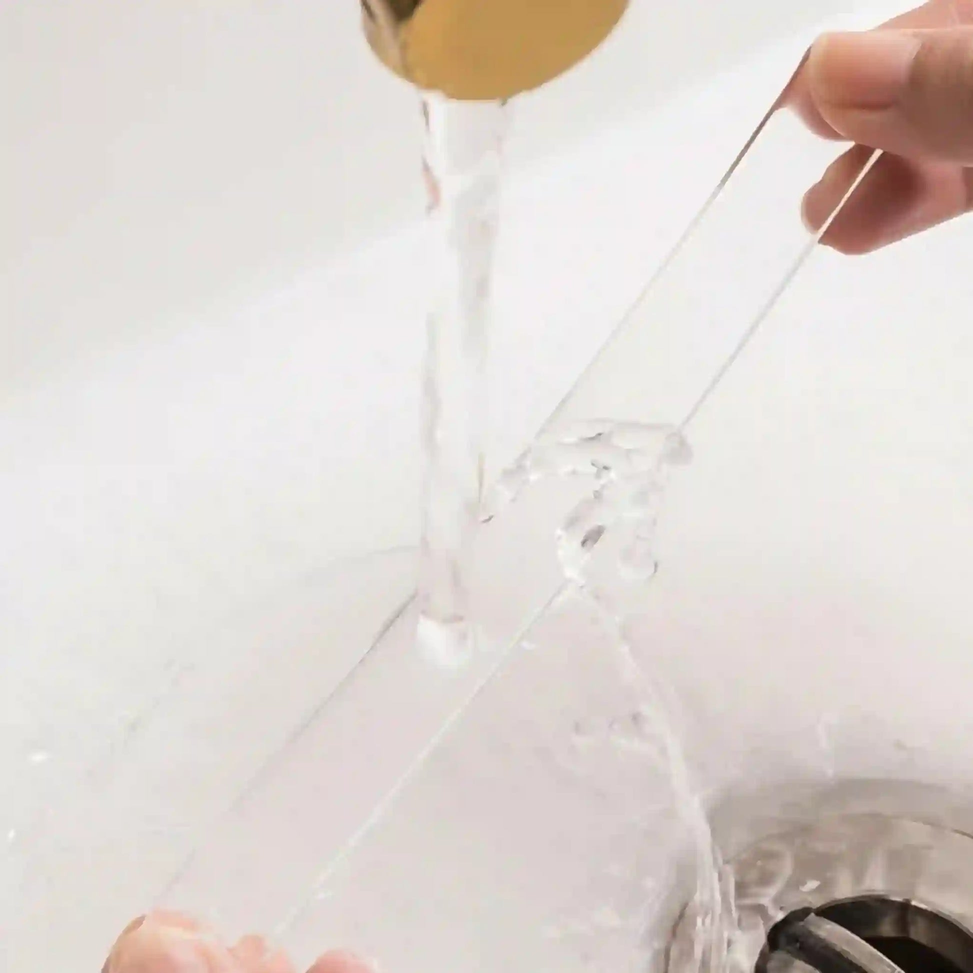 Clear plastic bag with a gold handle being held over a sink.