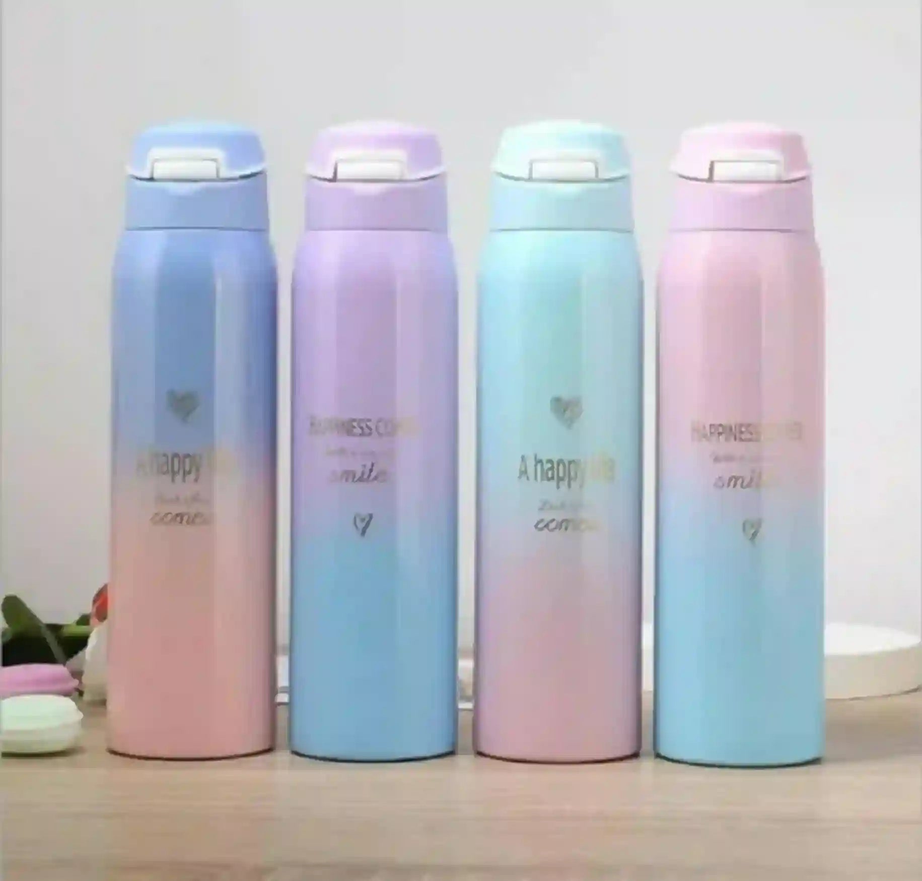 Four pastel-colored thermos bottles with gradient designs on a wooden surface.