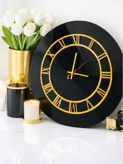 Black wall clock with gold Roman numerals on a decorative setting with flowers and candles.