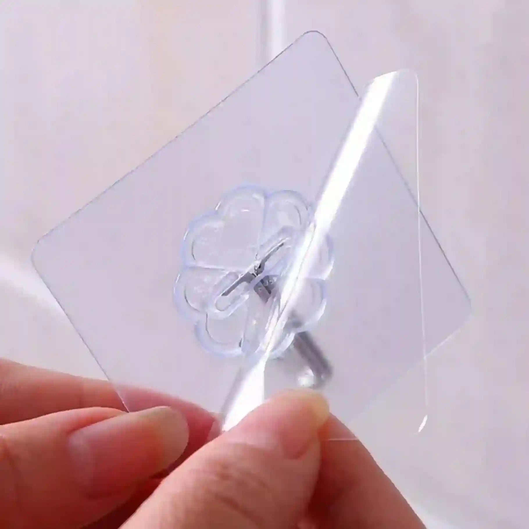Clear adhesive hook being applied to a white surface with a hand holding it.