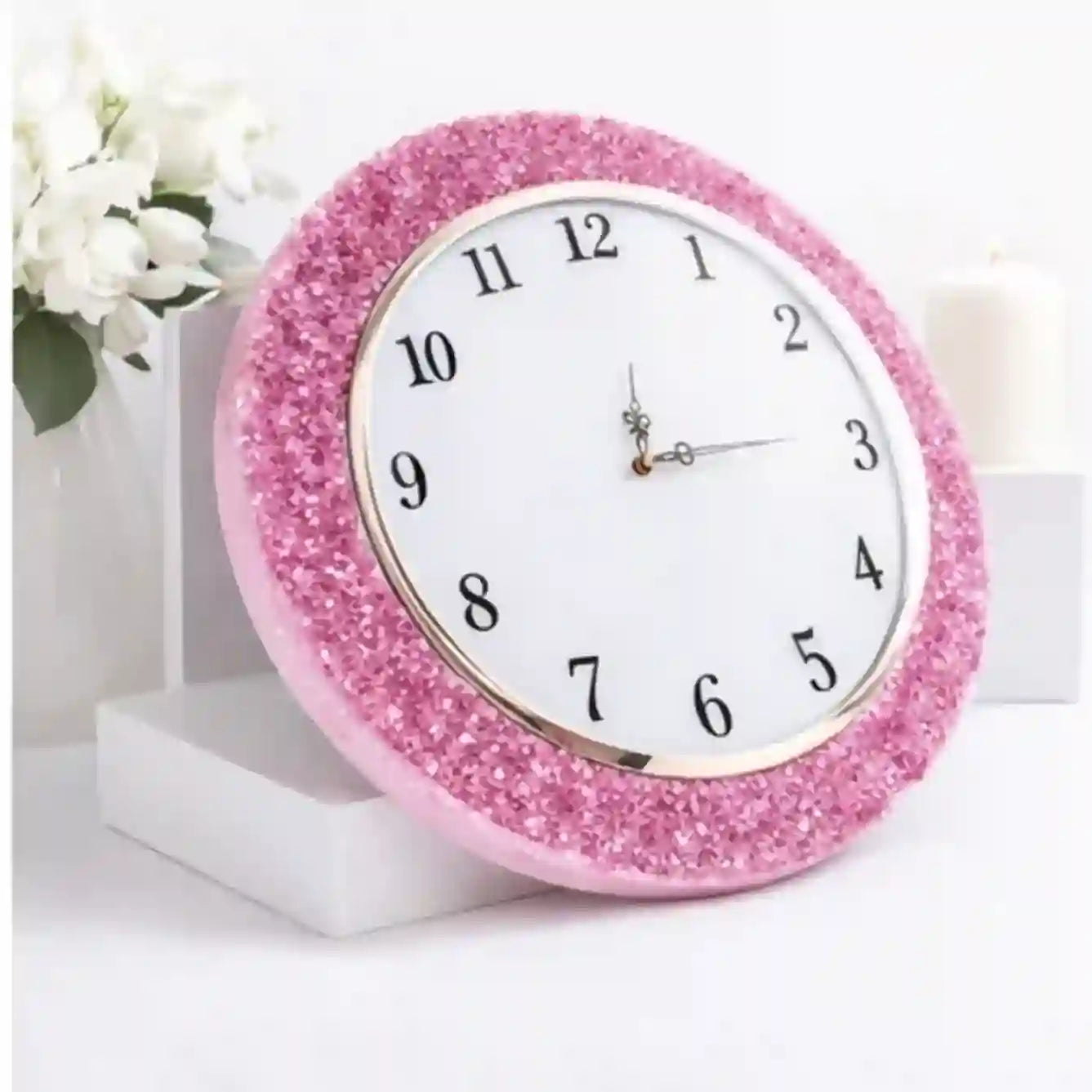 Pink glittery clock on a white surface with a floral background