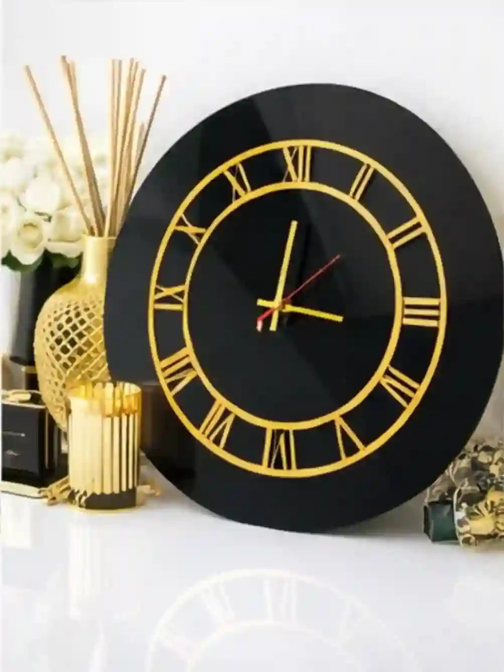 Black wall clock with gold Roman numerals on a white surface.