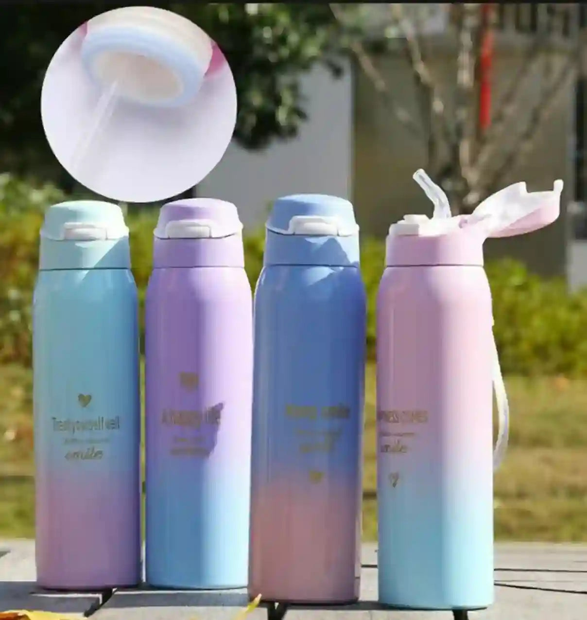 Four gradient-colored thermos bottles with straws on a blurred outdoor background