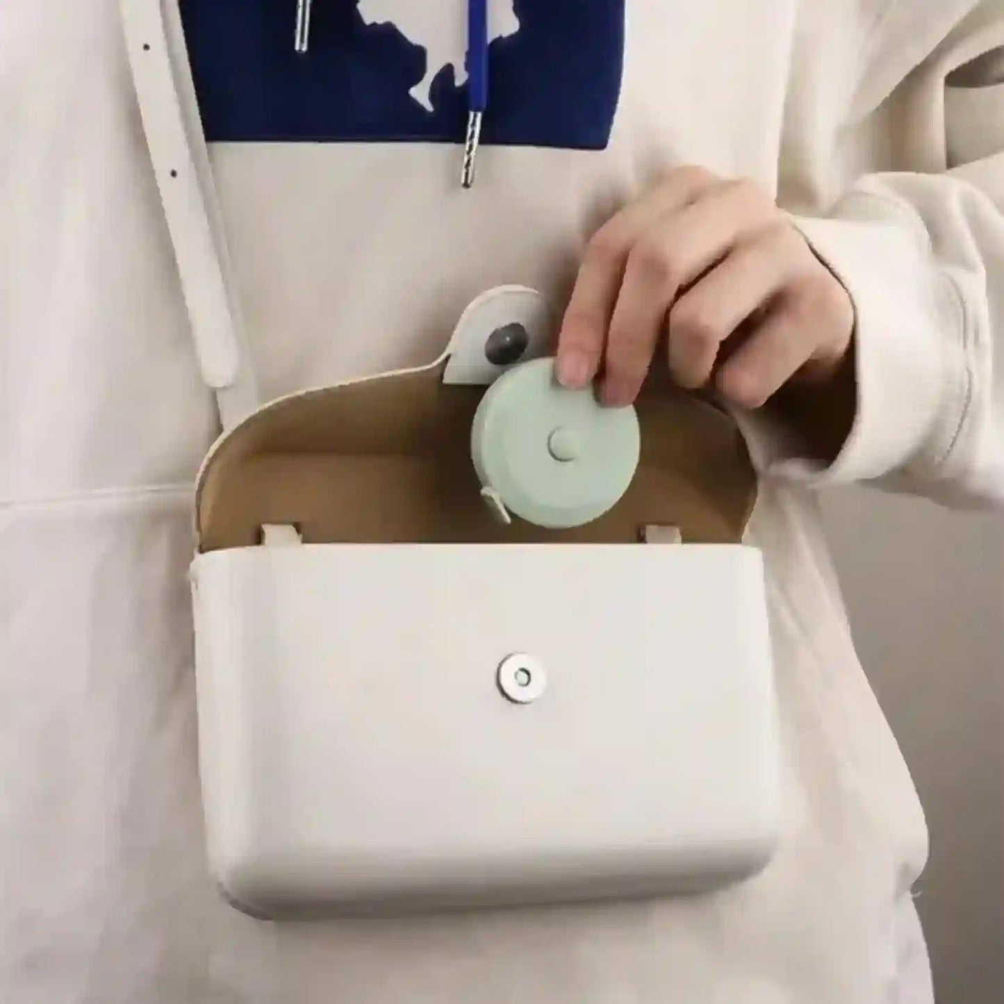 Person holding a small white bag with a green circular object inside, wearing a light-colored hoodie.