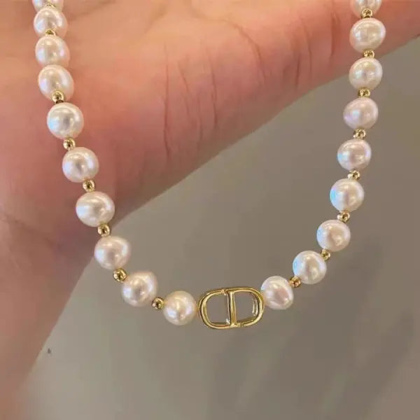 Pearl bracelet with gold clasp held by a hand against a neutral background
